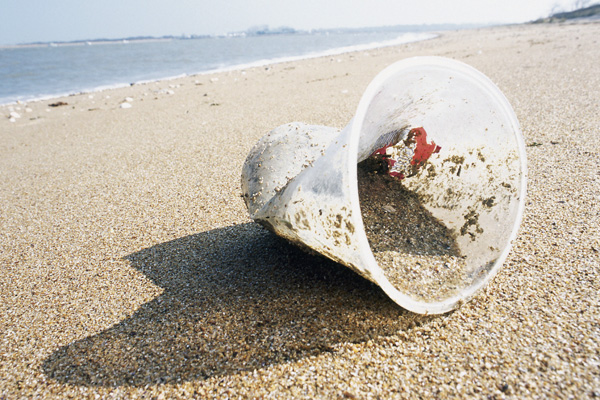Bild: Ein alter, zerknüllter Plastikbecher liegt im Sand am Strand